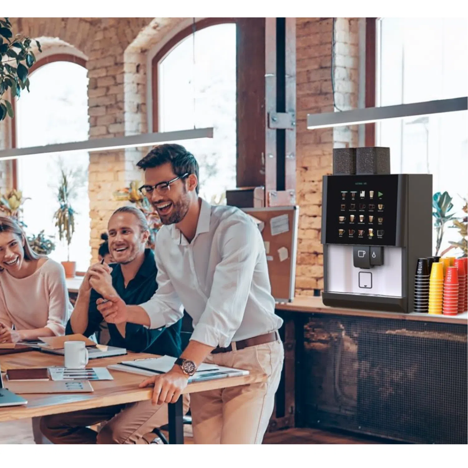 A diverse group of people sitting around a table inside a room with windows. They are smiling and engaged in conversation, dressed in various styles of clothing.